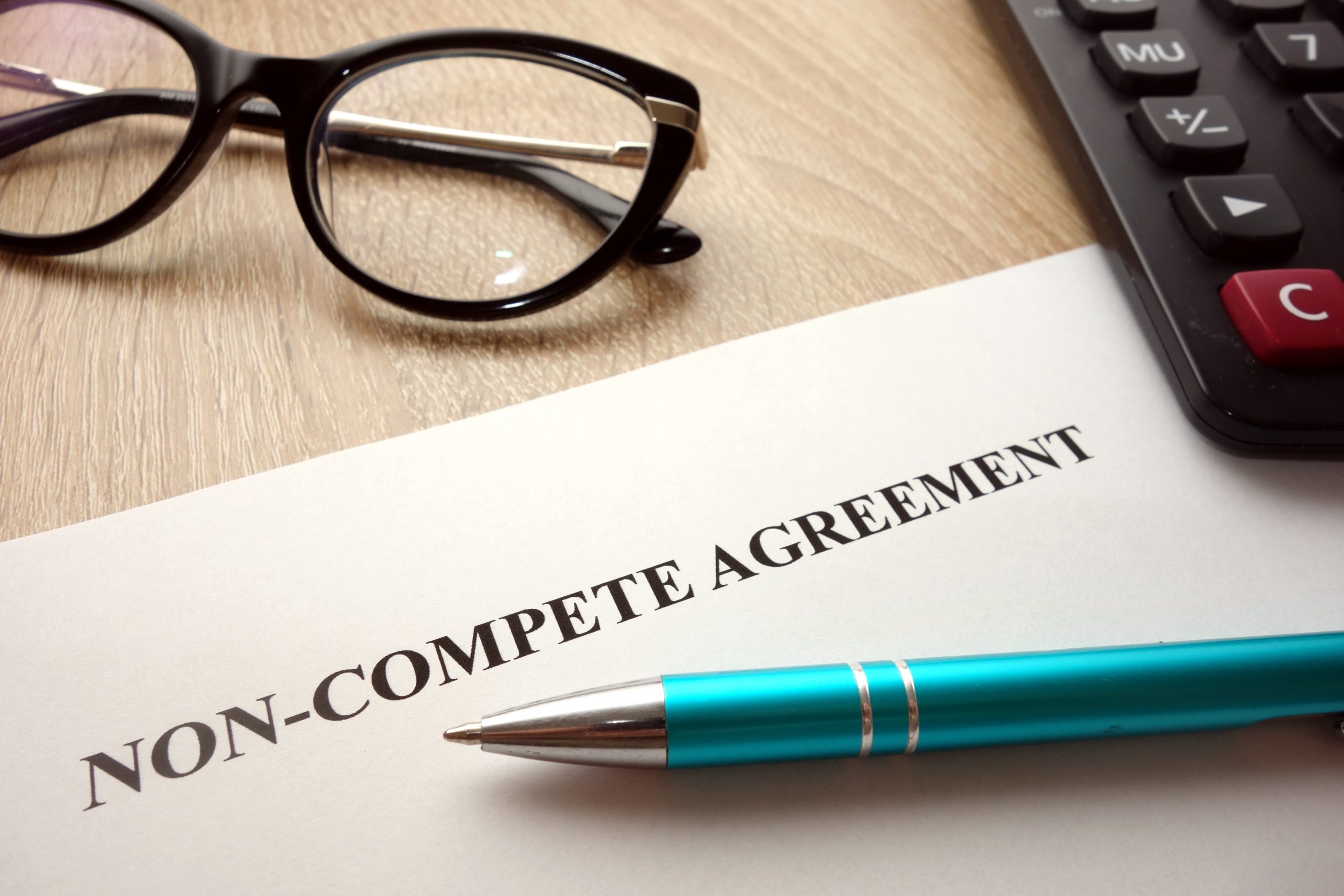 Photo of a desktop, pen, glasses and piece of paper with the title Non-Compete Agreement